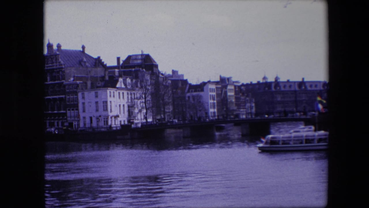 Tour boat on a canal near a bridge and rows of waterfront buildings.