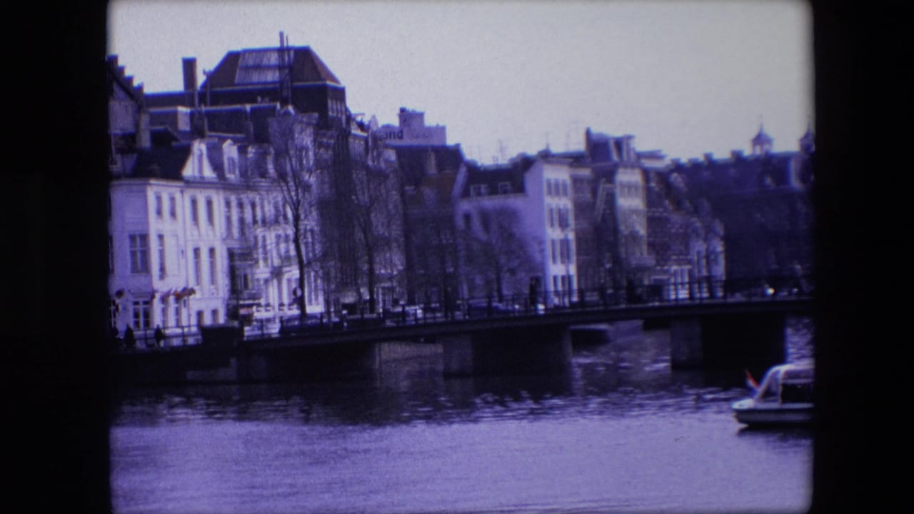Final frame from the 1967 Amsterdam canal clip, with waterfront architecture, a bridge over the canal, bare trees, and a cropped tour boat at right.
