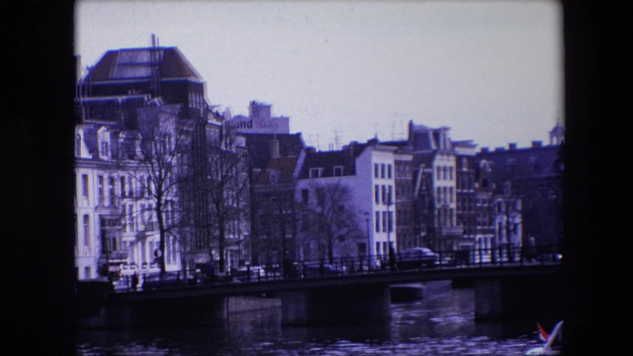Bridge over canal with waterfront buildings, bare trees, cars, and a small boat near the lower right.