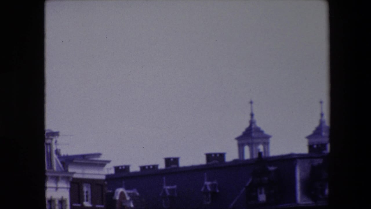 End frame from 1967 Amsterdam 8mm footage with the pan shifted right, leaving partial canal-house rooftops, chimneys, antennas, and two spired towers visible.