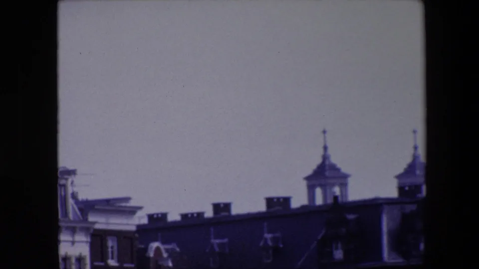 End frame from 1967 Amsterdam 8mm footage with the pan shifted right, leaving partial canal-house rooftops, chimneys, antennas, and two spired towers visible.
