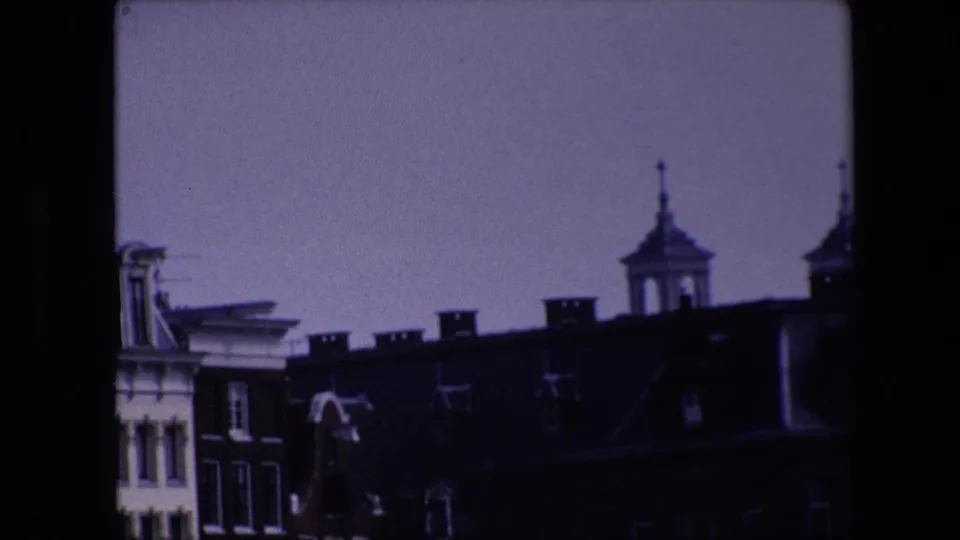 1967 Amsterdam frame with a purple cast, dark roofline, cupola tower, chimneys, and partial historic facade within visible 8mm borders.