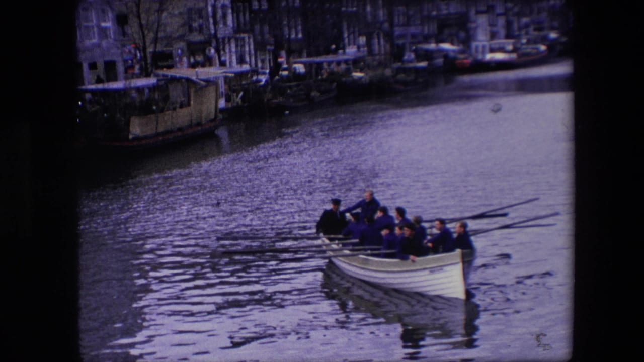 A crew rows a white boat on rippled canal water near moored boats.