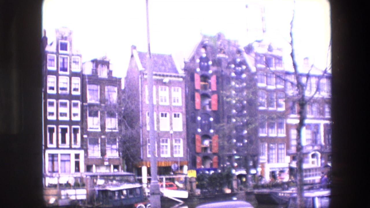 Gabled canal houses with boats along the waterfront and bare tree branches in front.