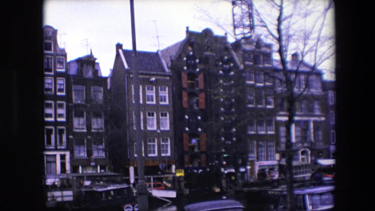 1967 Amsterdam frame showing canal-front brick buildings, a moored boat, bare trees, and a partial vehicle along the lower edge.