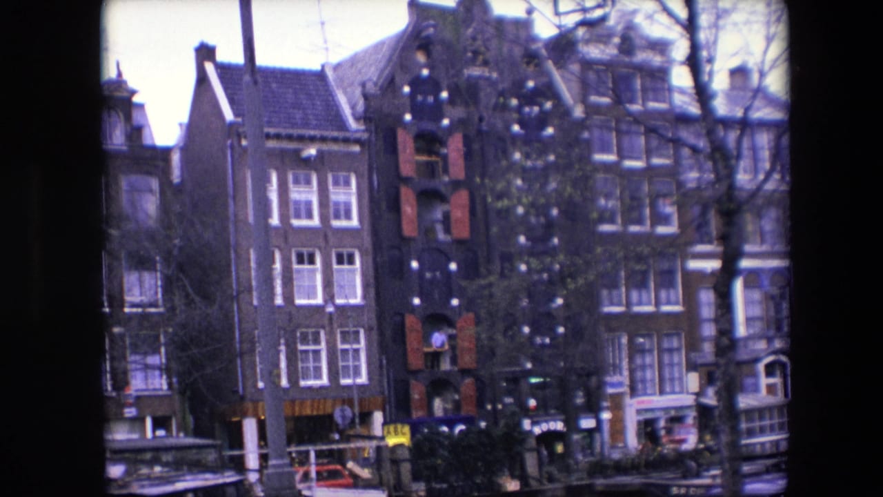 Closer 1967 view of Amsterdam brick canal houses with red shutters, a decorated exterior, bare trees crossing the frame, moored boats, and small street-level figures.