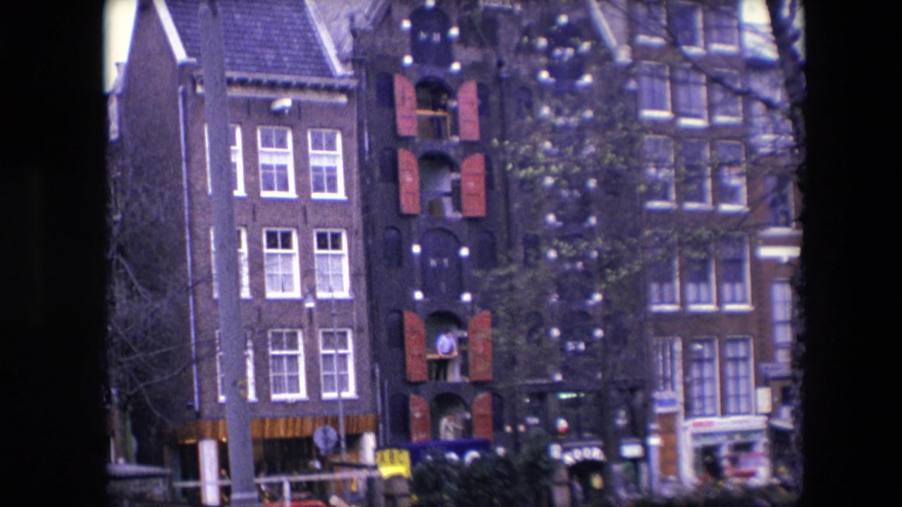 Final frame of the 1967 Amsterdam canal view, centered on a decorated brick building with red shutters, adjacent historic facades, boats below, bare tree branches, and indistinct people or signage at street level.
