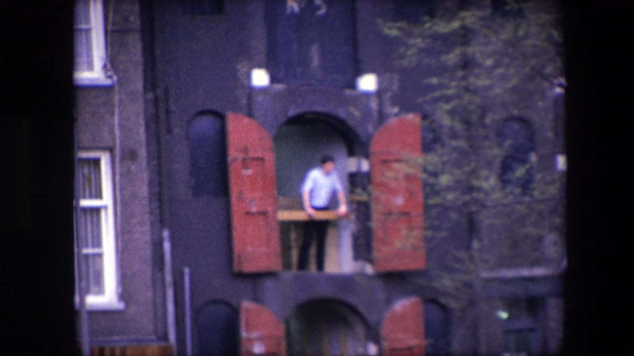 1967 Amsterdam frame with a man at an upper-level opening, red shutters swung outward, and a dark masonry facade partly obscured by nearby foliage.