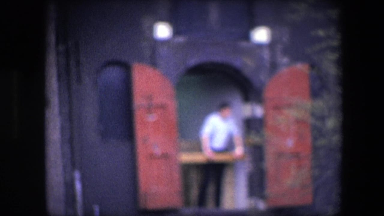 Man standing at the same balcony opening with red shutters on both sides.