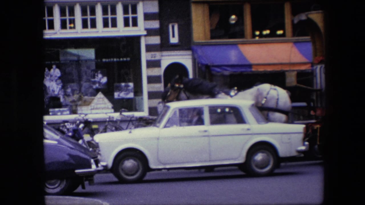 A white classic car crosses the frame in the Amsterdam street scene, partially obscuring the waiting horse cart near bicycles, pedestrians, and Dutch storefronts.