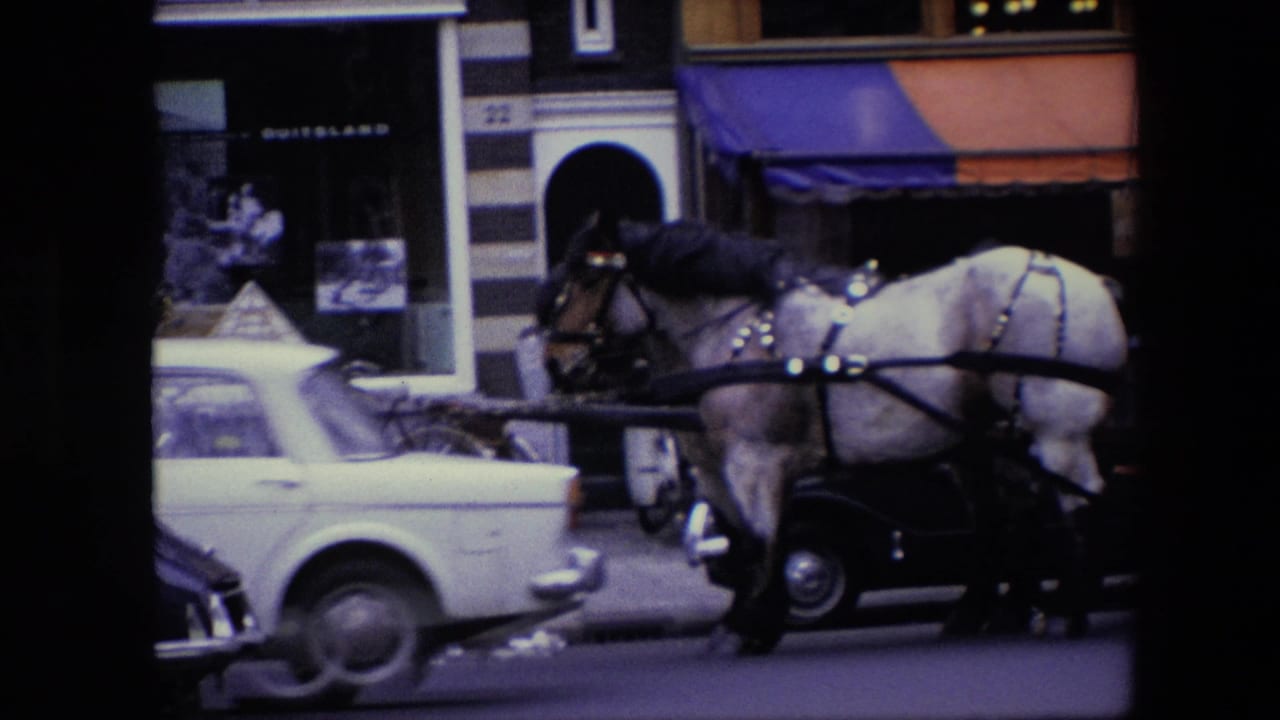 1967 Amsterdam street view with a harnessed horse and carriage passing cars in front of striped storefronts and shop windows.