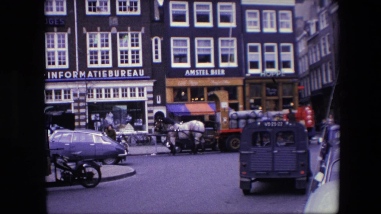 1967 Amsterdam street frame showing pedestrians near storefronts, a horse-drawn wagon loaded with barrels, a blue Volkswagen Beetle, a motorcycle, and a dark utility van in traffic.