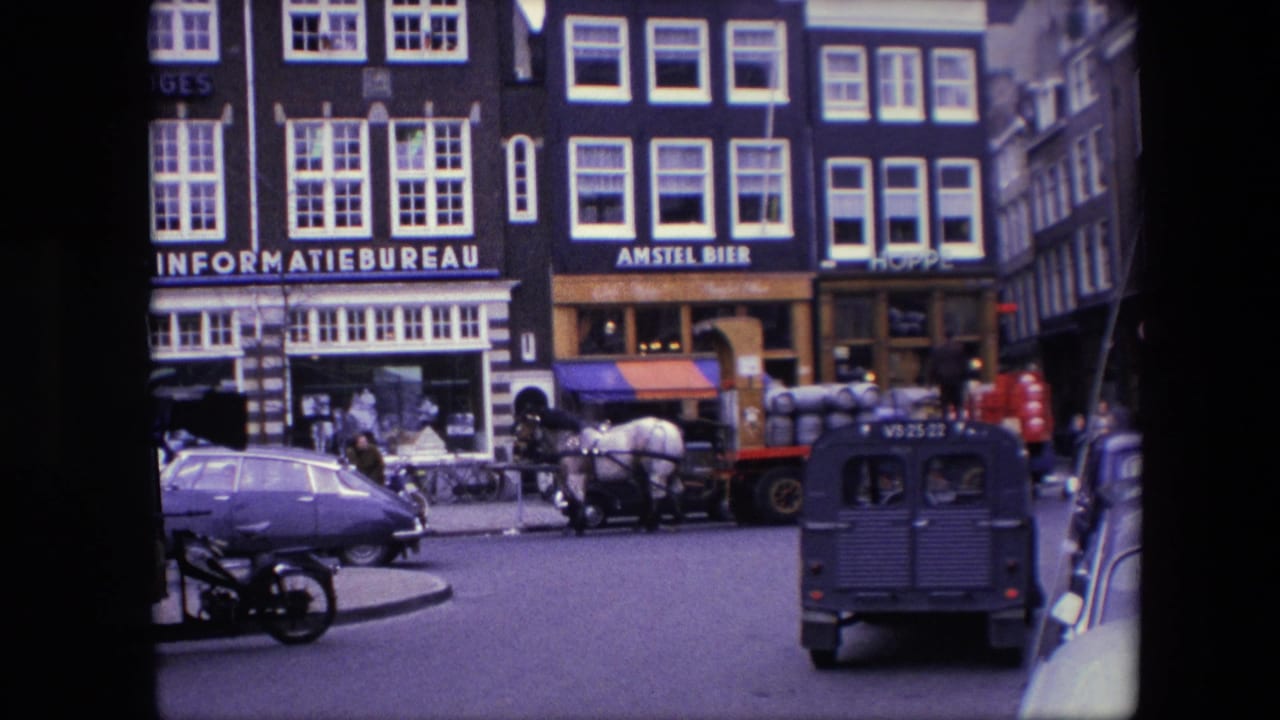 1967 Amsterdam street view with tall storefront buildings, readable INFORMATIEBUREAU and AMSTEL BIER signs, pedestrians, a horse-drawn barrel wagon, a Volkswagen Beetle, and a small utility van.