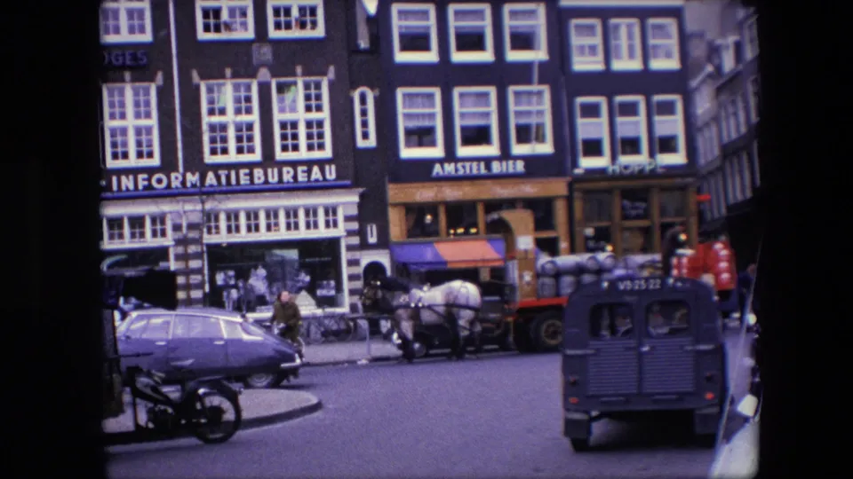 1967 Amsterdam curbside view showing a purple sedan in the foreground, a horse-drawn delivery cart, a dark van, pedestrians, and Dutch streetfront buildings.