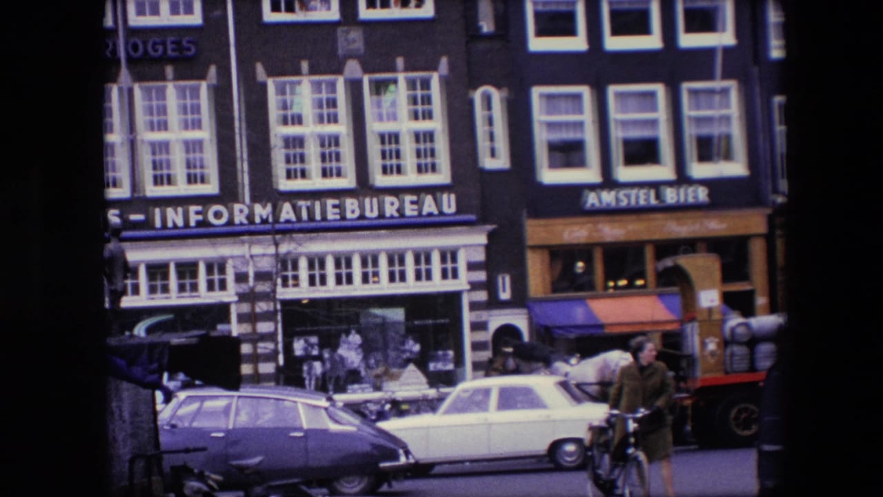 1967 Amsterdam street frame with Stichting Reis - Informatiebureau and Amstel Bier storefronts, a white car, a purple car, a cyclist, and a horse-drawn cart partly visible.