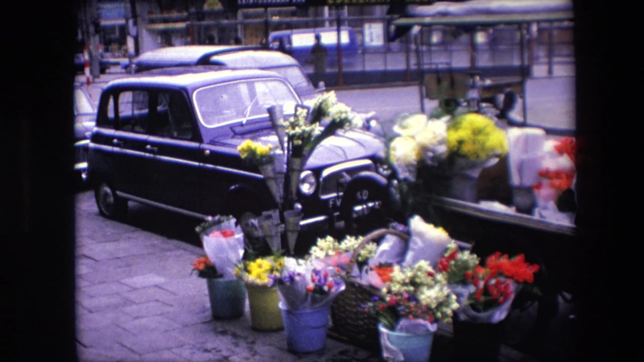 Clearer 1967 Amsterdam frame showing a black car parked next to a flower stall with colorful bouquets in buckets and baskets.