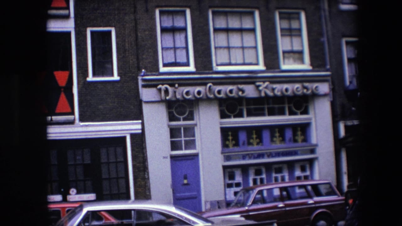 Street-level 8mm view of a building exterior with Nicolaas Kroese lettering, purple door, multiple windows, and parked cars in Amsterdam, supported by 1967 clip metadata.