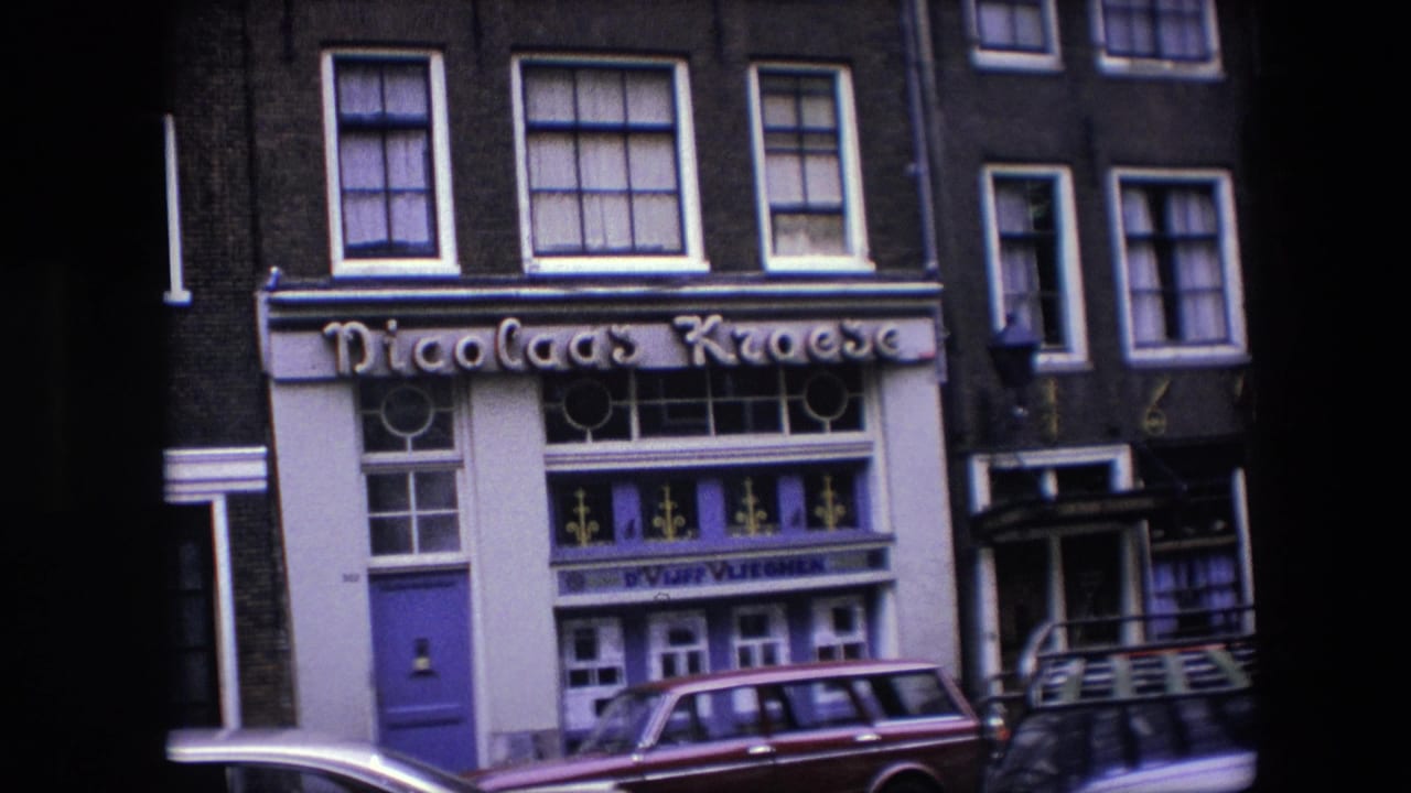 1967 Amsterdam frame of the Nicolaas Kroese exterior, showing the storefront sign, purple and white facade details, upper-floor windows, and a maroon station wagon parked outside.