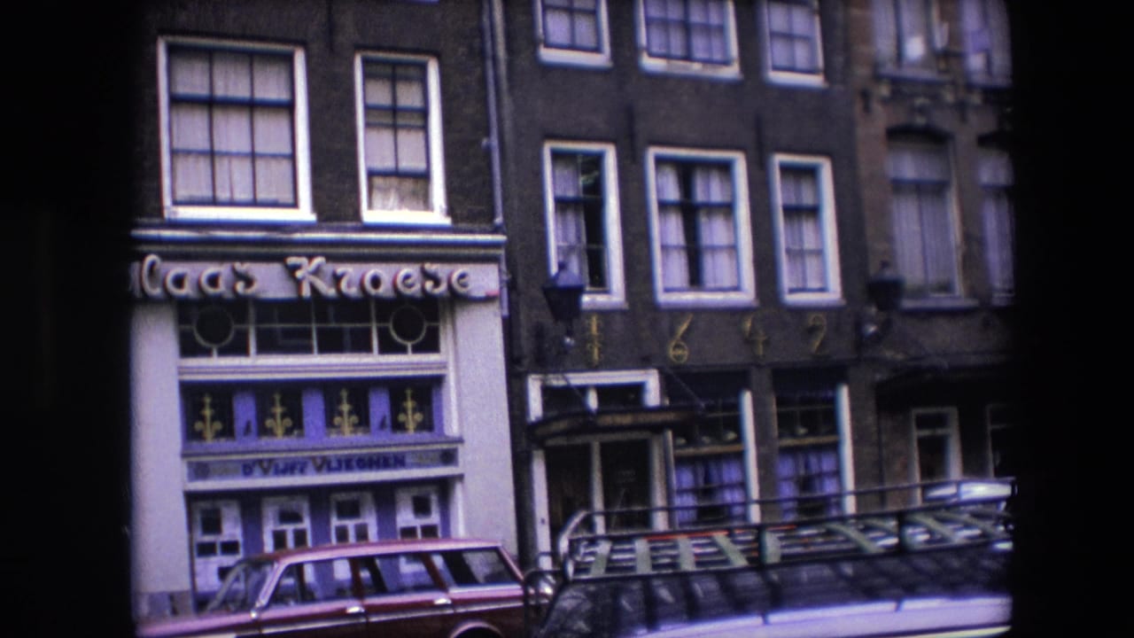 1967 Amsterdam frame showing a partial view of the Nicolaas Kroese sign and storefront beside neighboring building details, upper windows, and cars along the street.