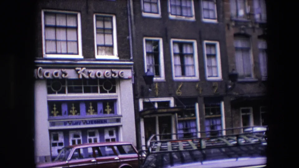 1967 Amsterdam frame showing a partial view of the Nicolaas Kroese sign and storefront beside neighboring building details, upper windows, and cars along the street.