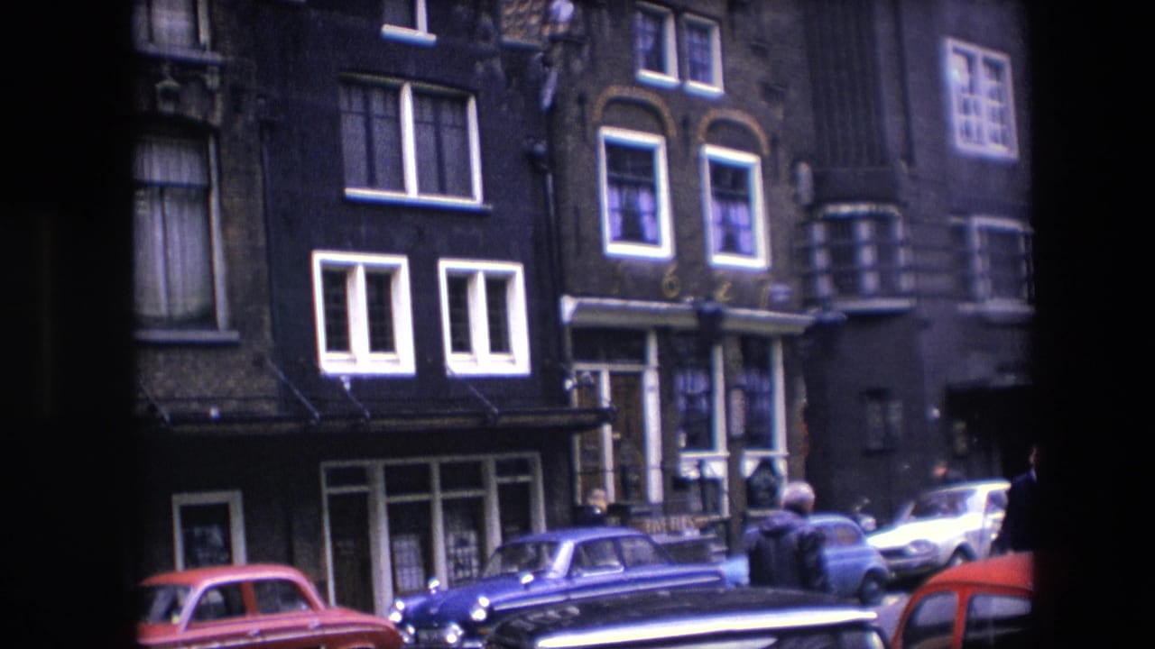1967 Amsterdam street view showing pedestrians near parked cars, narrow multi-story buildings, white-framed windows, and a partial passing vehicle at the edge of frame.