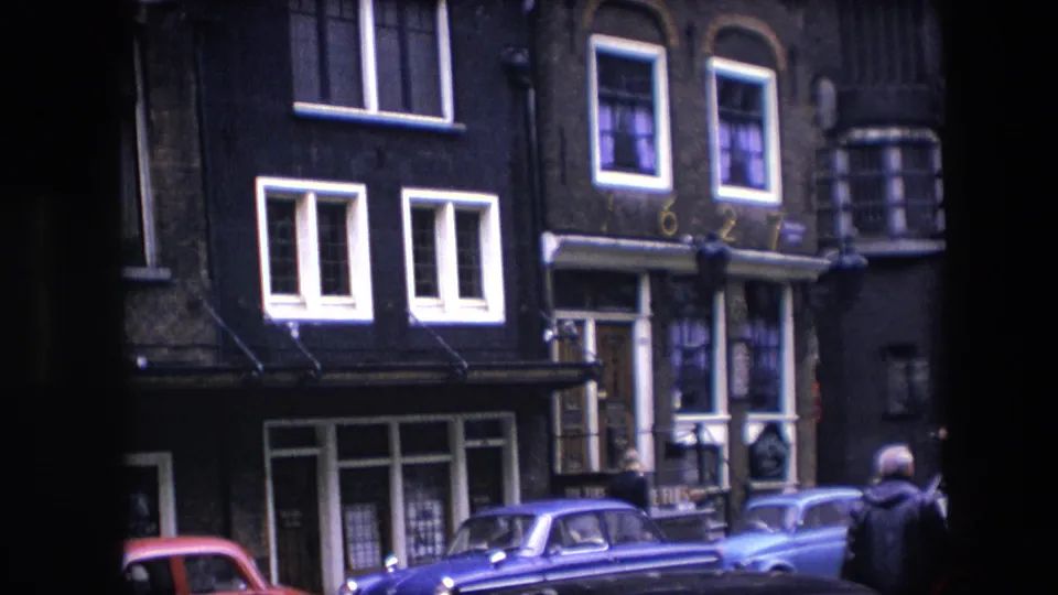 Amsterdam street facade identified by metadata as 1967, with dark brick buildings, white-framed windows, and parked red, blue, and gray cars along the curb.