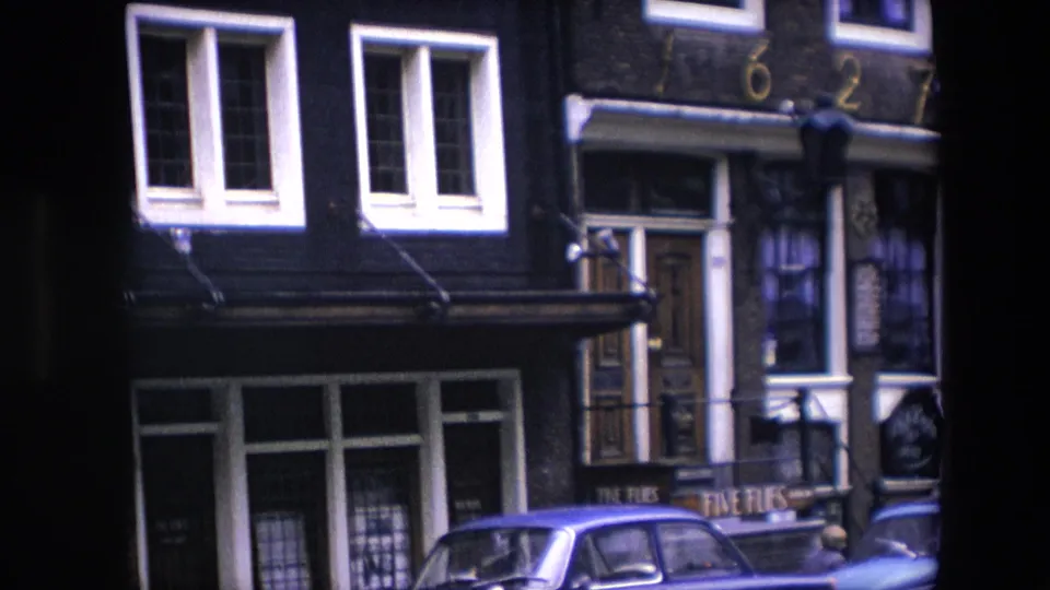 Closer 1967 Amsterdam street detail, with white-trimmed windows, a doorway below address numerals, shopfront glass, and a blue car parked at the curb.