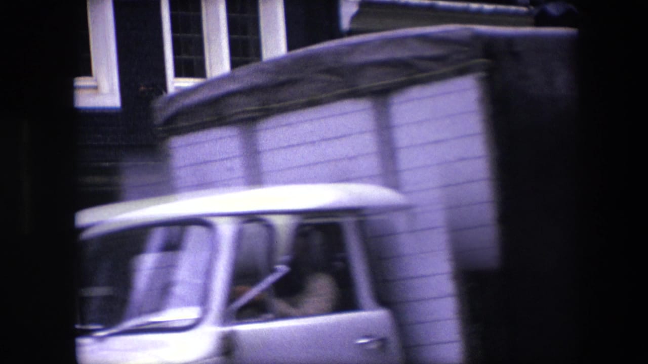 A light-colored van or truck passes across the 1967 Amsterdam street view, partially obscuring the brick building and parked cars behind it.