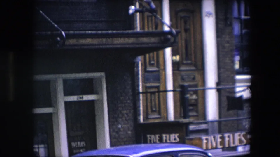 1967 8mm frame identified as Amsterdam, showing the Five Flies sign beside an ornate wooden doorway with a blue car roof crossing the lower frame.