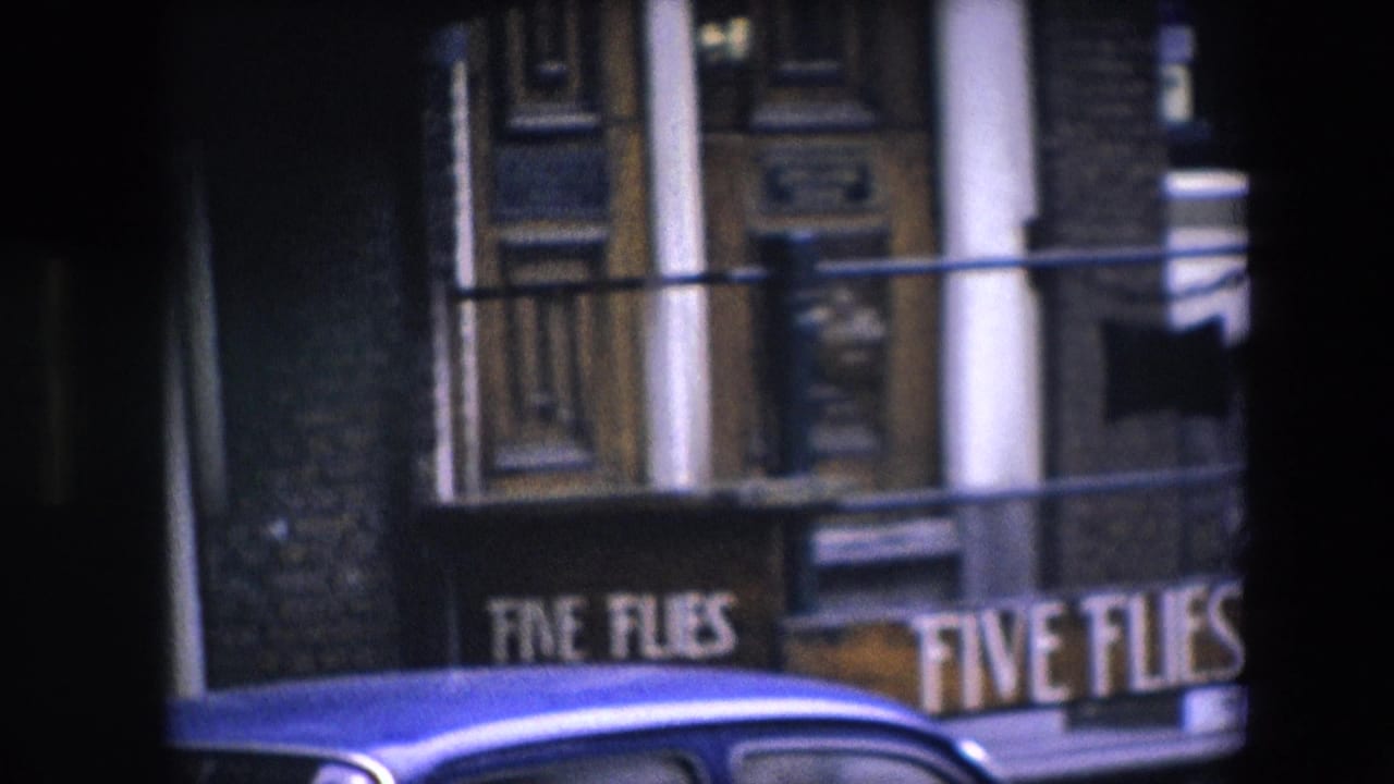 1967 8mm frame identified as Amsterdam, showing a closer home-movie view of the Five Flies sign below a dark facade, with white columns and a blue car in the foreground.