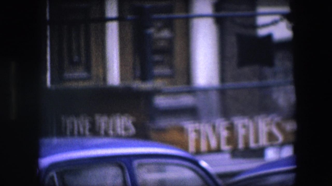 1967 8mm frame identified as Amsterdam, showing a soft close view of the Five Flies sign, the blue car roof, and ornate entrance details behind railings.