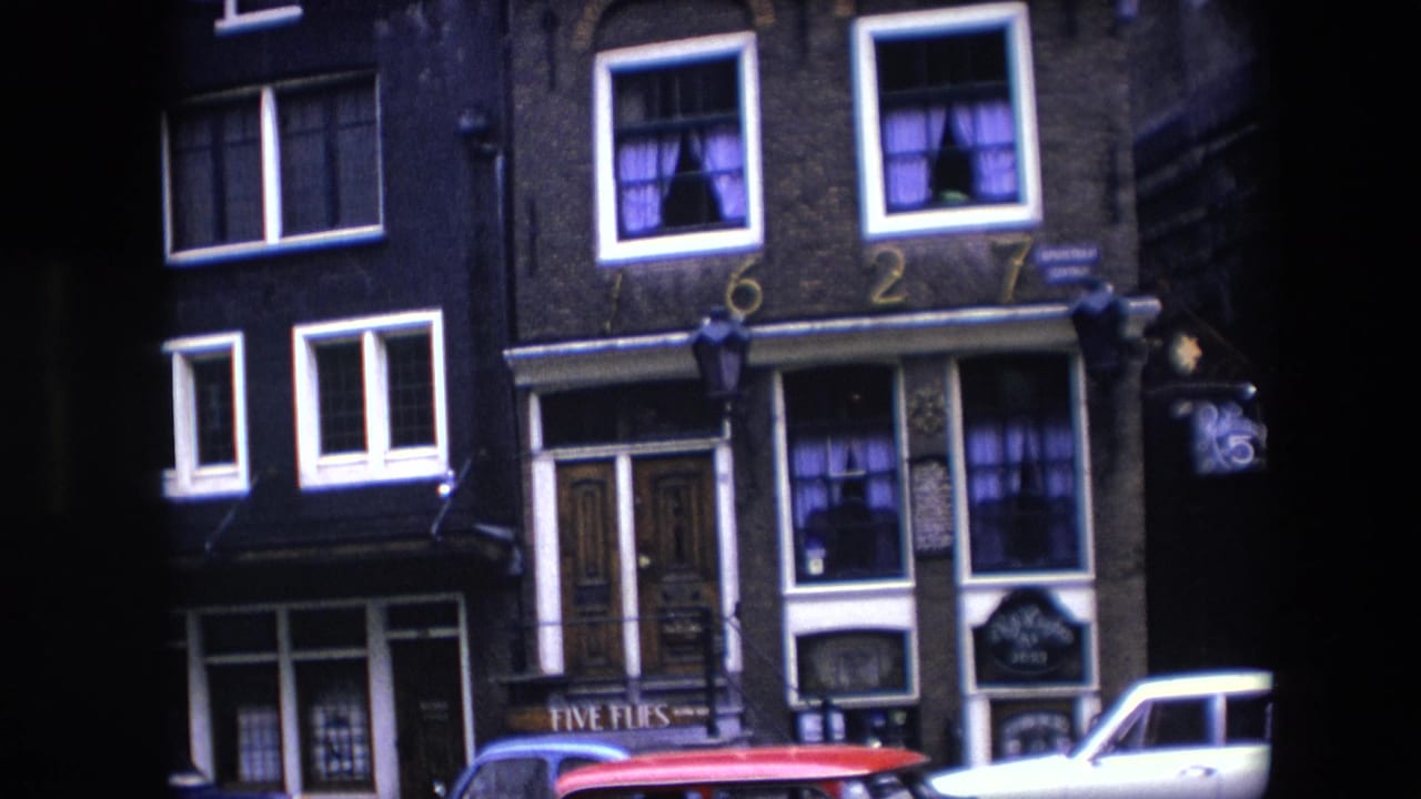 1967 Amsterdam street view of a narrow brick facade with white-trimmed windows, purple curtains, painted 1627 numerals, a hanging lamp, and partial red and white cars below.