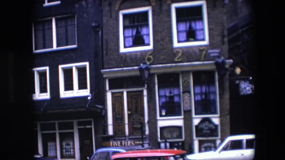 1967 Amsterdam street view of a narrow brick facade with white-trimmed windows, purple curtains, painted 1627 numerals, a hanging lamp, and partial red and white cars below.