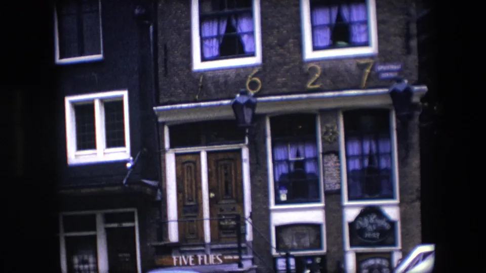 1967 Amsterdam facade detail showing the brick building front, painted 1627 numerals, white-trimmed windows, purple curtains, hanging lamps, and Five Flies signage near the doorway.