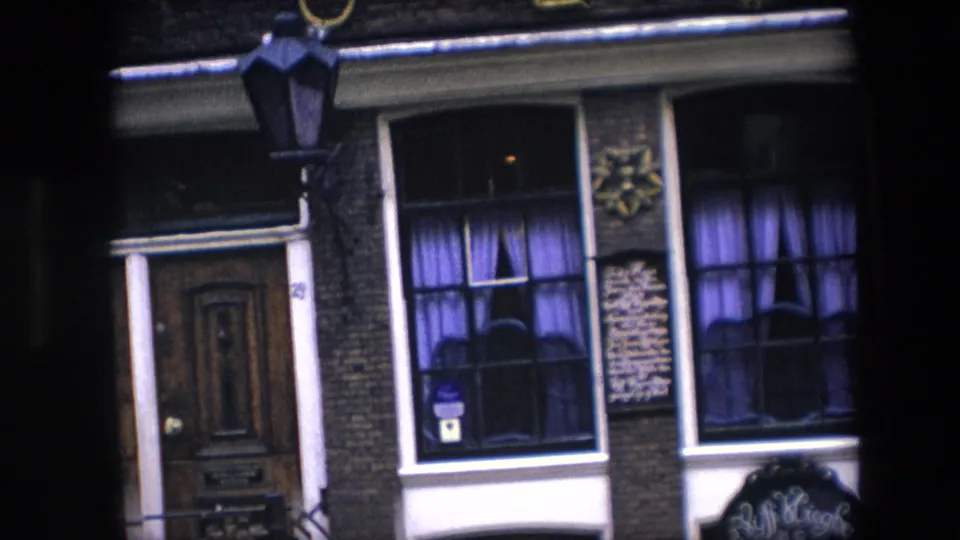 1967 Amsterdam close facade view with a wooden door, purple-curtained windows, a hanging street lamp, wall-mounted signs, and partial 1627 numerals along the upper edge.