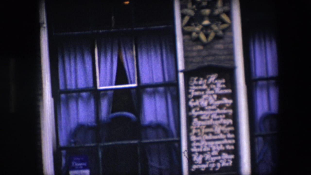 Closer 1967 Amsterdam frame of a nighttime facade with tall curtained windows, white writing on dark wall panels, vertical pipes, and decorative star-like plaques above.