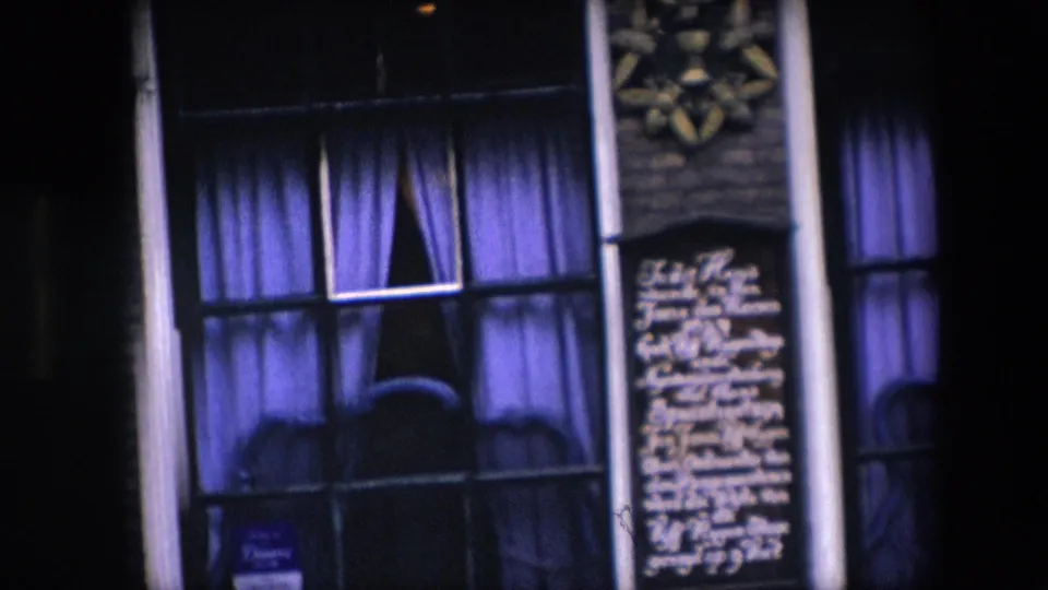 Closer 1967 Amsterdam frame of a nighttime facade with tall curtained windows, white writing on dark wall panels, vertical pipes, and decorative star-like plaques above.