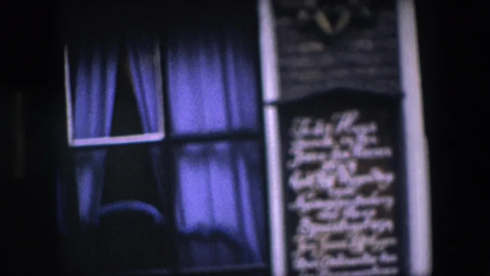 Soft 8mm close-up from the Amsterdam facade showing purple curtains behind a window, dark brickwork, a vertical pipe, and blurred white writing on the wall.