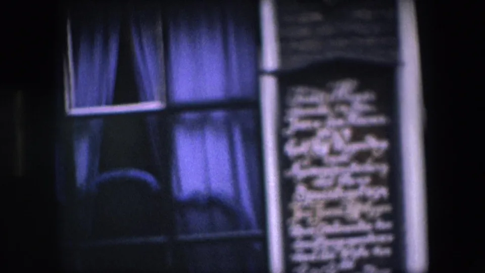 Close 1967 Amsterdam frame with a purple-curtained window and a neighboring dark wall panel filled with white lettering, partly softened by handheld focus and nighttime exposure.