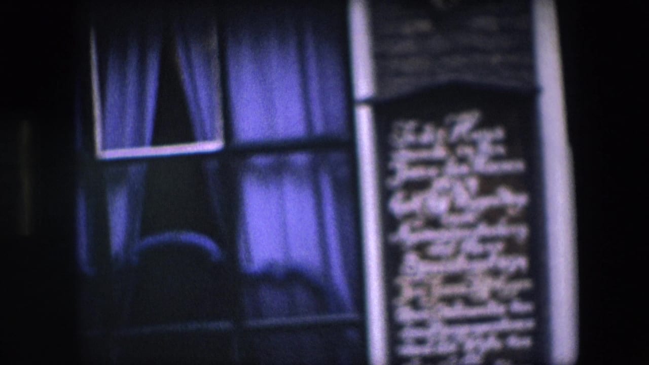 Close 8mm frame of a dark Amsterdam brick facade with a white-trimmed window, blue-purple curtains, and a commemorative plaque at the side.