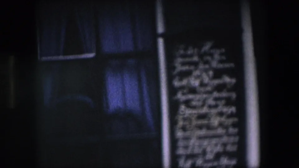 Dark, underexposed 8mm frame showing a curtained window and blurred commemorative plaque on the same brick facade.