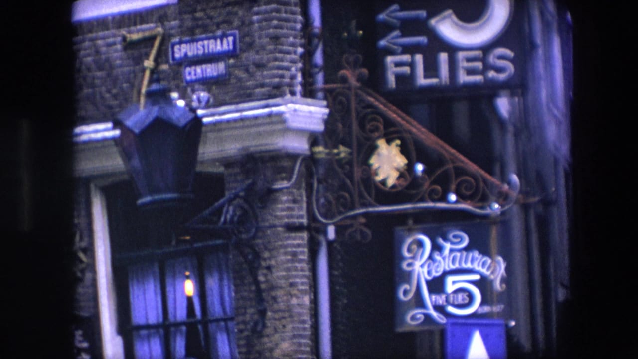 1967 8mm frame of an Amsterdam brick building entrance showing Dutch street signs, wrought iron scrollwork, and the illuminated Restaurant Five Flies sign at night.