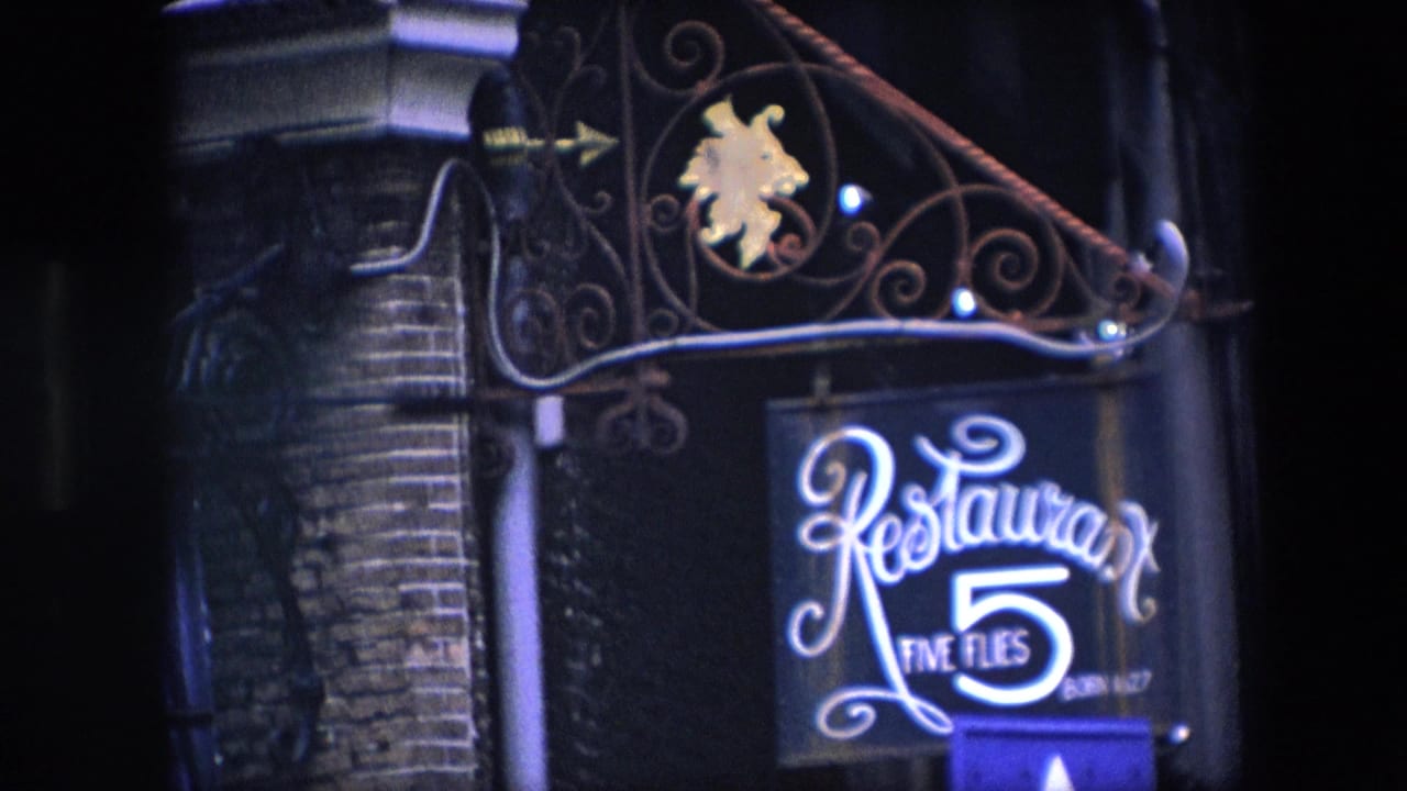 Closer night view of the Restaurant Five Flies sign hanging from a brick facade.
