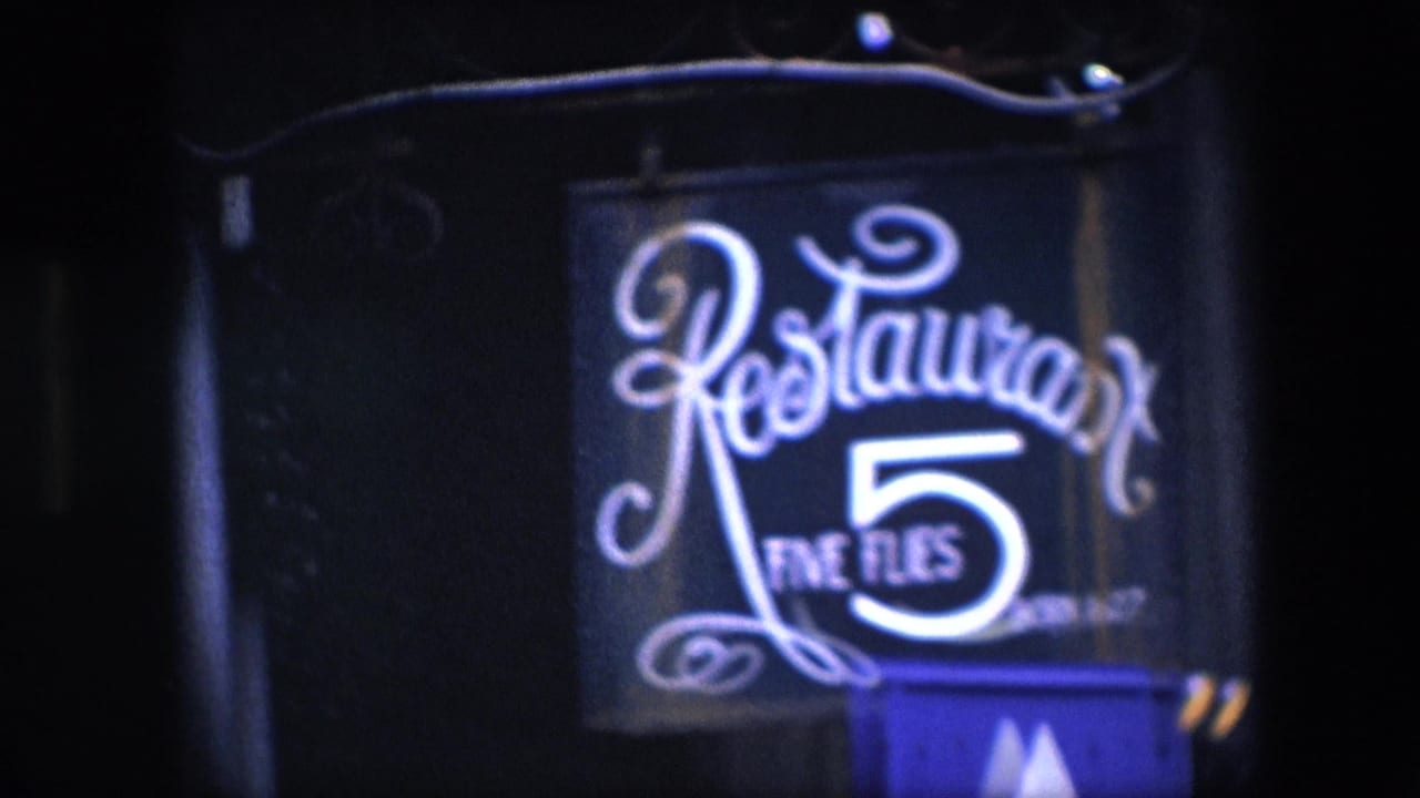 1967 Amsterdam 8mm frame showing the illuminated Restaurant Five Flies exterior sign, with ornate cursive lettering, a bright numeral 5, and a dark building facade around it.