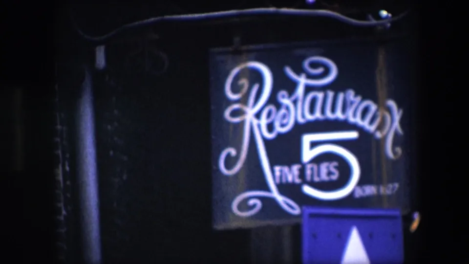 1967 Amsterdam 8mm frame with the Restaurant Five Flies sign centered in low light, showing the white numeral 5, cursive restaurant lettering, and metal sign support.