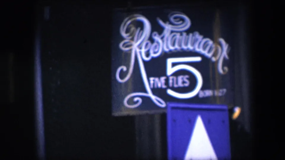 1967 Amsterdam 8mm frame showing a closer handheld view of the Restaurant Five Flies sign, with ornate script, bright number 5, and a blue panel beneath the sign.