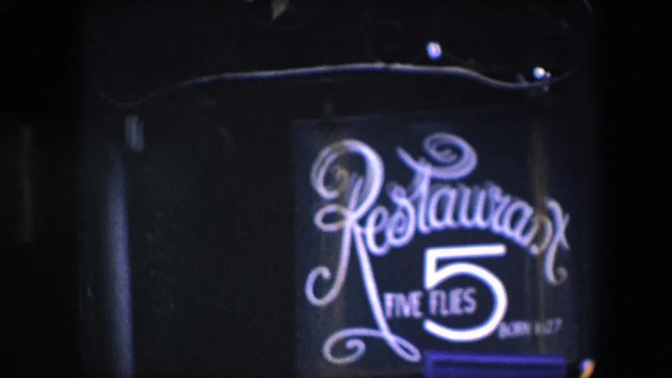 1967 Amsterdam 8mm frame showing the Restaurant Five Flies sign in soft focus, with the bright numeral 5 and cursive lettering glowing against a dark street-facing facade.