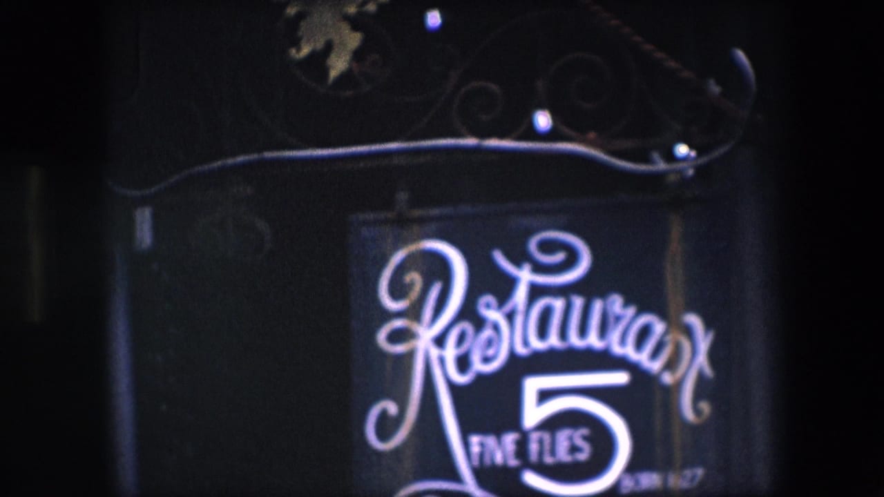 1967 Amsterdam home-movie frame showing a glowing Restaurant Five Flies sign with cursive lettering and a large number 5 on a dark facade.