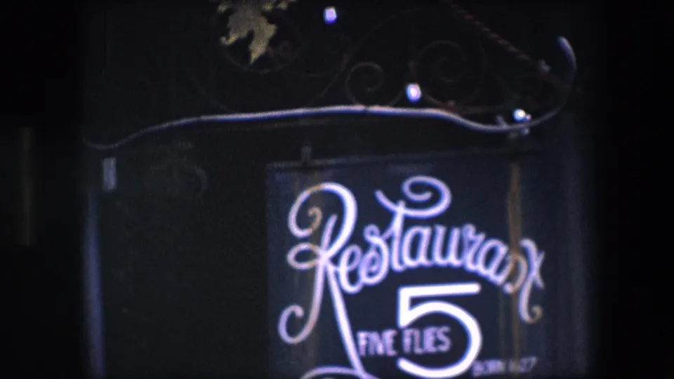 1967 Amsterdam home-movie frame showing a glowing Restaurant Five Flies sign with cursive lettering and a large number 5 on a dark facade.