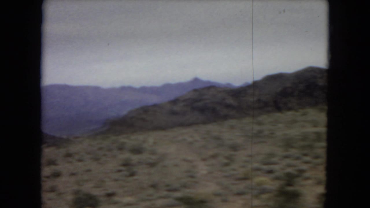 Desert hillside and distant mountains seen from a moving car.